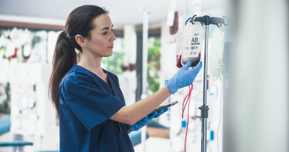 Female Nurse Holding Tablet Computer And Checking The Blood Bag In Donation Center.