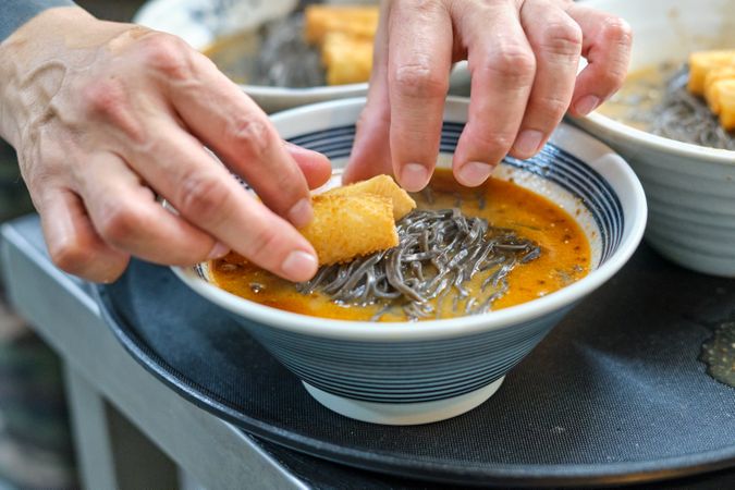 Cook preparing noodle soup with crispy chicken skin