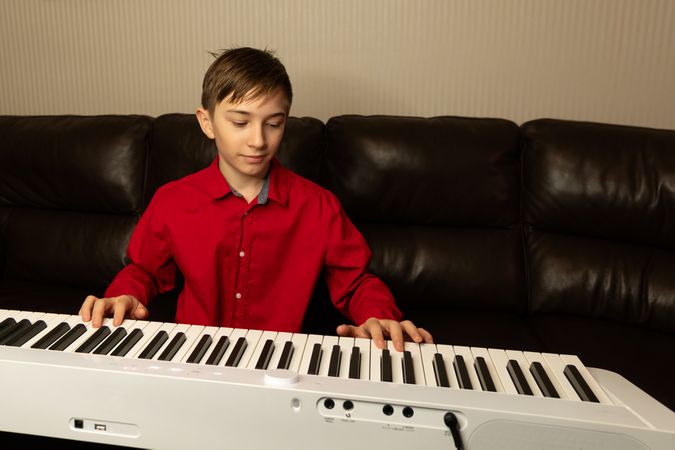 Boy playing piano with focused expression on face.