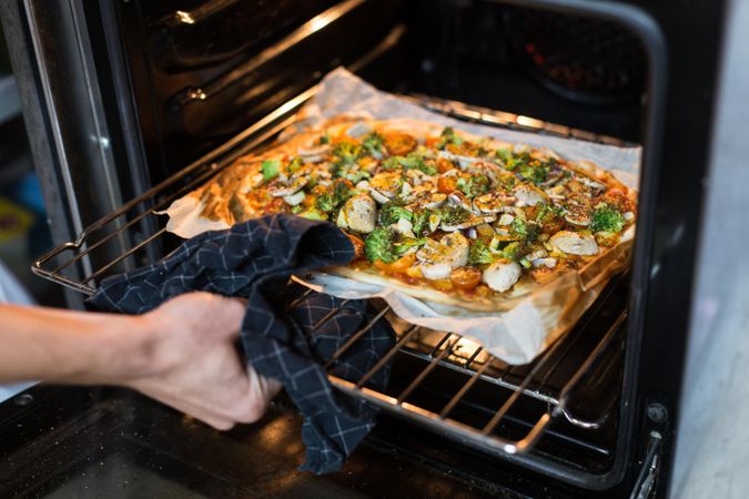 Hand taking pizza out of oven