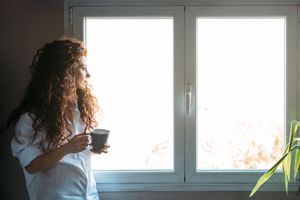 Woman standing by a windows with a cup of coffee