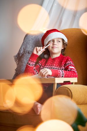 Dreamy child in Santa hat drawing in armchair