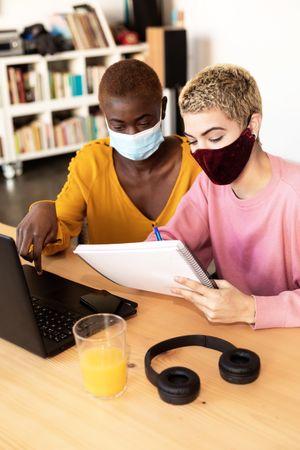 Female friends working together at laptop wearing protective masks