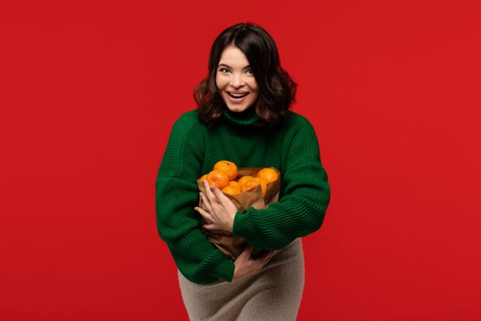 Woman in green sweater hugging paper bag full of tangerines