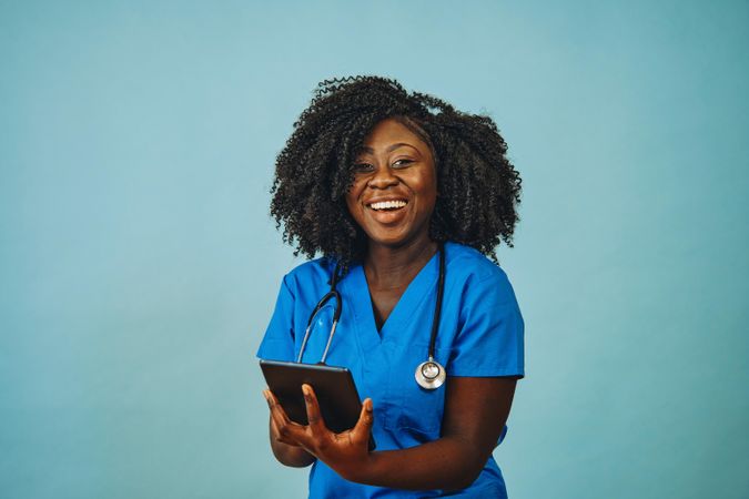 Portrait of laughing Black medical professional dressed in scrubs with tablet