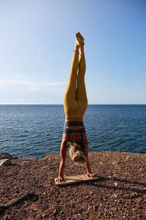 Slim sportswoman taking Handstand pose at seaside