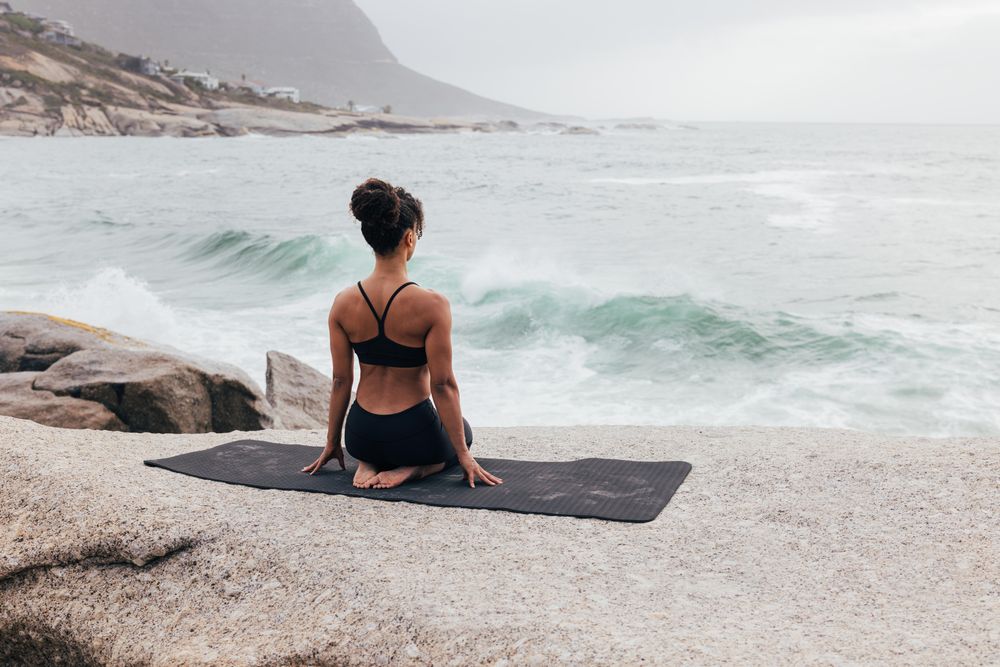 Female sitting next to the ocean sitting on knees enjoying the view