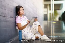 Woman sitting with digital tablet leaning against wall outside 41xwg5