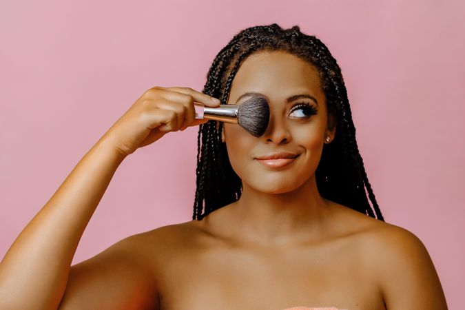 Black woman holding make up brush over her eye and looking away