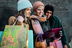 Three happy friends looking at a smartphone together after shopping.