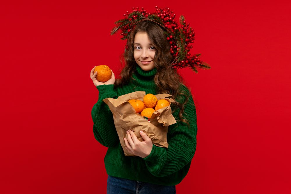 Young girl in green sweater holding oranges in paper bag