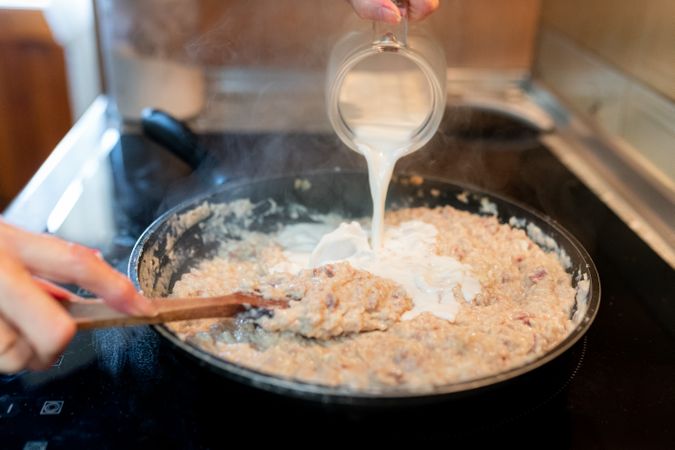 Person adding milk to the croquette dough in a pan