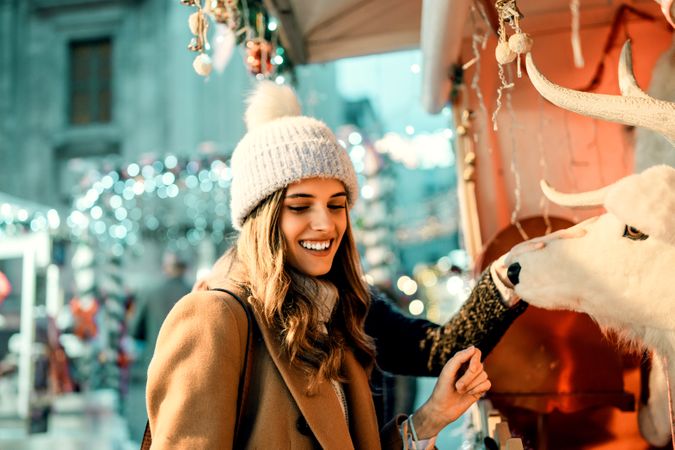 Young woman playfully interacting with a large reindeer decoration at a Christmas market.