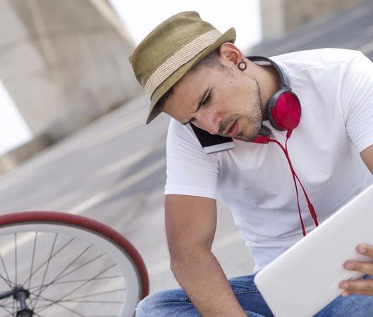 Man in hat speaking on phone and using laptop outdoors