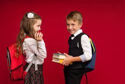 Preteens in school uniform carry backpacks on vivid red colored background