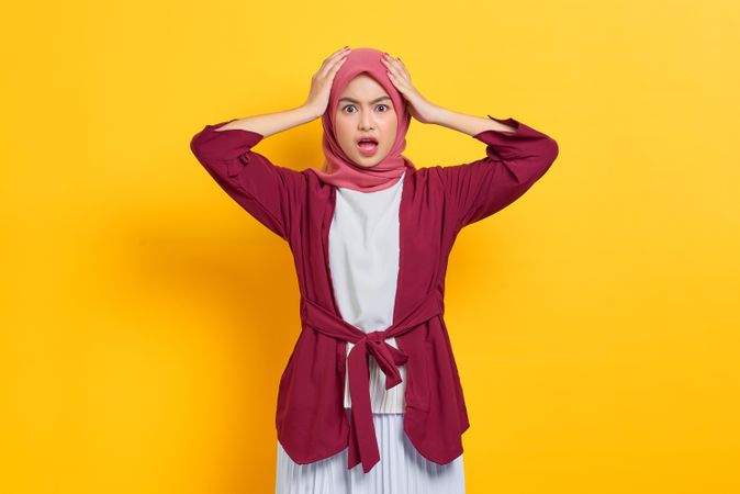 Shocked woman in red headscarf with hands on head looking at camera