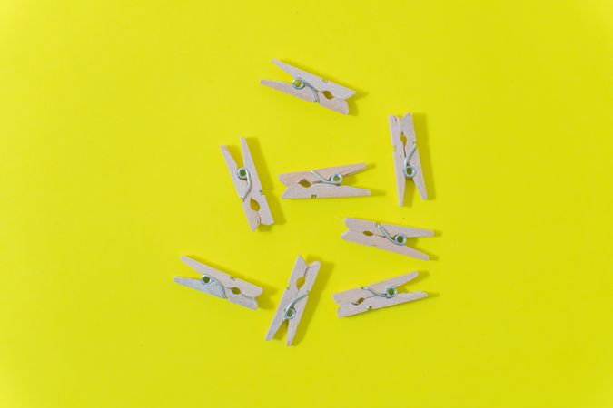 Flat lay of scattered wooden clothespins on a yellow surface