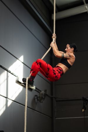 Side view of woman climbing rope in a gym