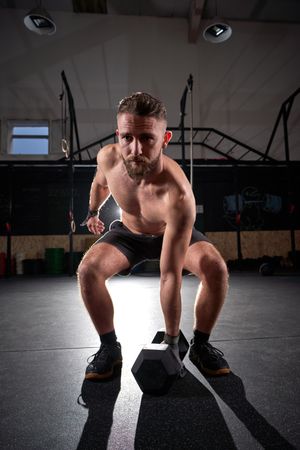 Muscular athlete training with hexagon dumbbell in fitness club