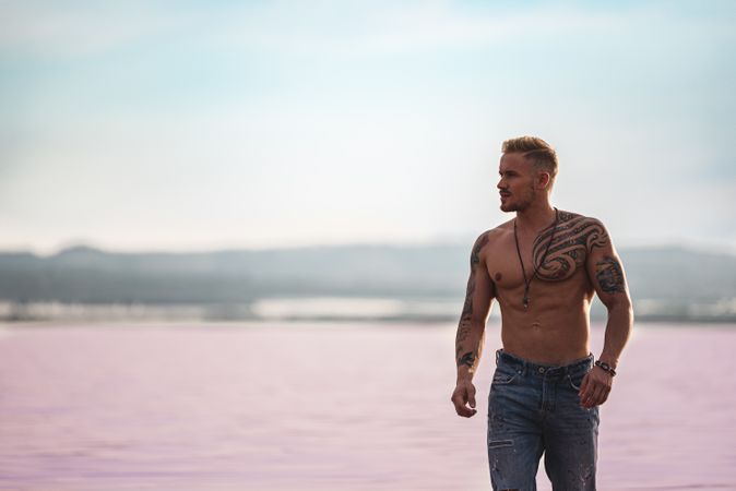 Undressed muscular man walking on shore of pink lake