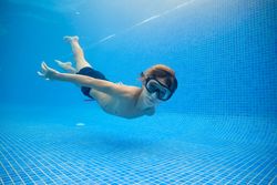 Boy in shirts and goggles swimming in blue pool