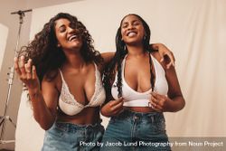 Two happy female friends wearing denim jeans and bras against studio background beLkp4
