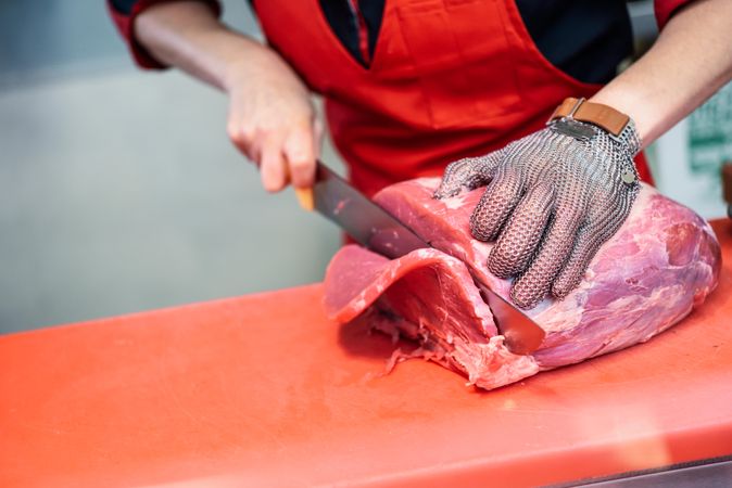 Close up of butcher in apron slicing raw meat