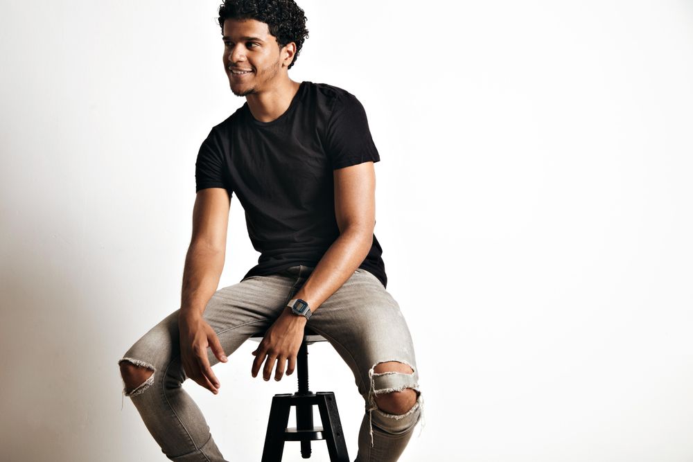 Smiling male model sitting on stool in studio shoot looking away from camera