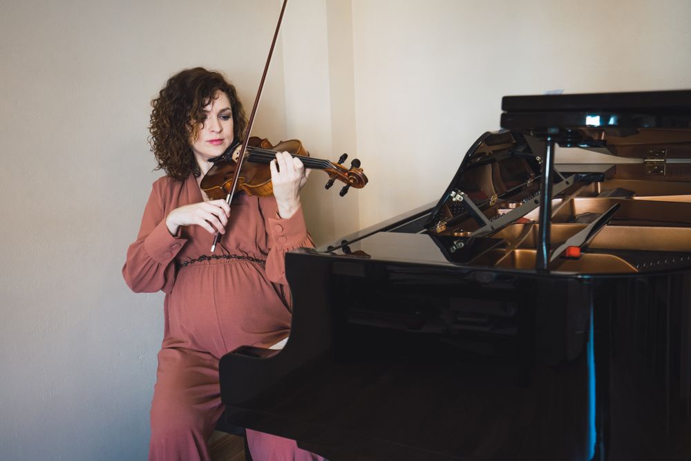 Pregnant woman playing on violin near piano in room