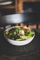Healthy vegetarian bowl pictured on table with dark chair with smoothie on side, copy space