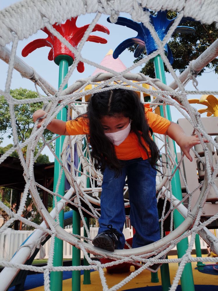 Girl with facemask standing in a climbing net at the playground