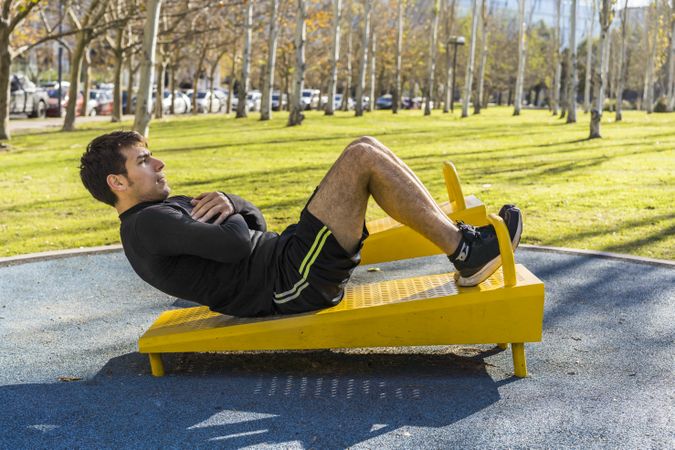 young man doing abdominal exercises on a public equipment in outdoor fitness