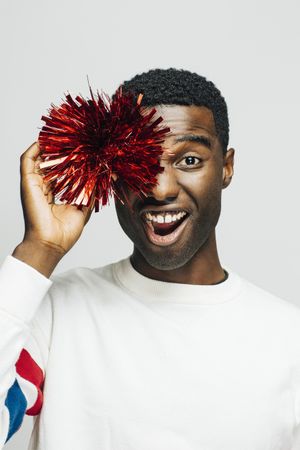 Black man making funny face while holding a pompom to his eye