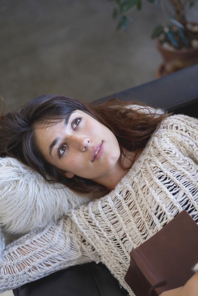 Portrait of woman lying on sofa with book on her chest, vertical