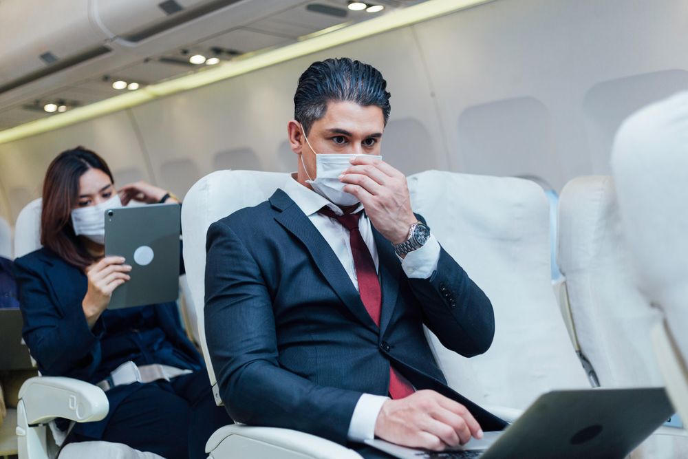 Male and female sitting on rows in airplane using tablet and laptop