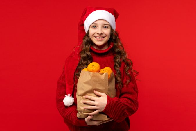 Happy girl in Santa hat holds bag of oranges