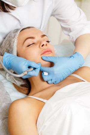 Woman having facial beauty treatment with machine on her jawline, vertical
