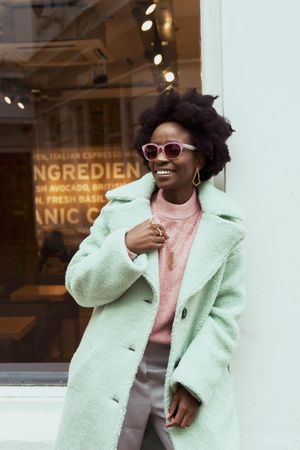 Smiling woman in teal coat wearing sunglasses standing outdoor