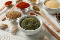 Close up of of wooden scoop full of peppercorn with bowls of spice