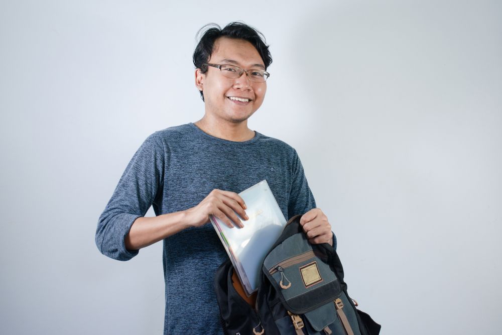 Asian student male looking for book in bag with happy gesture