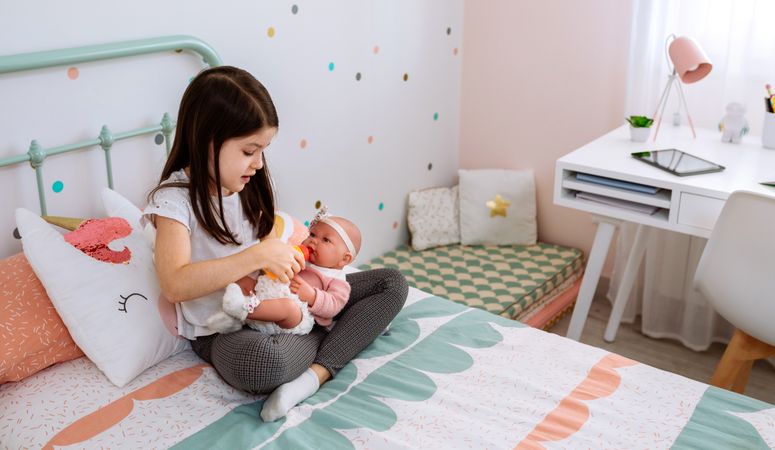 Little girl playing with her baby doll and leaving the tablet on the desk