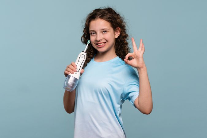 Girl showing OK sign with electric toothbrush.