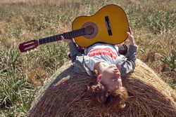 Carefree boy with guitar lying on hay bale in meadow