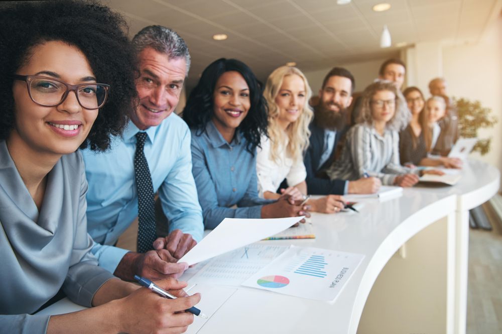 Multi-ethnic group of people in office attire smiling in a row at work