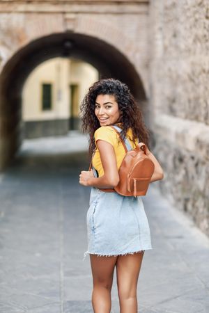 Happy Arab woman walking outside towards arch, vertical