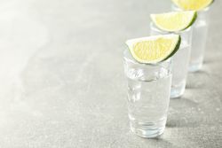 Tequila shots with lime slices on grey background
