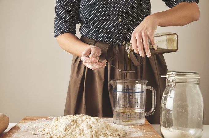 Woman pouring olive oil into a spoon with a pile of dough