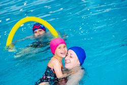 Cheerful girl swimming in pool with mother