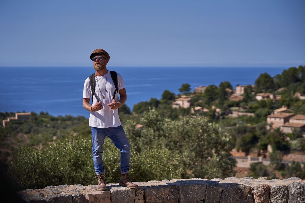 Unemotional male tourist in sunglasses standing on stony wall against sea