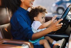 Woman sitting in car with cute little boy on lap